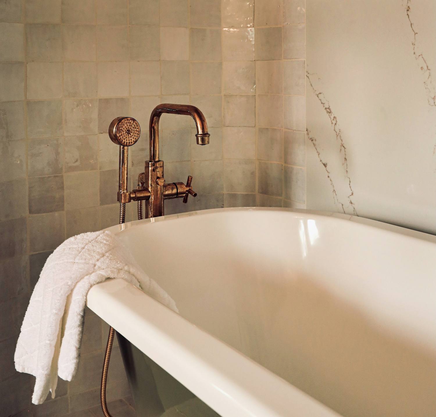 Freestanding soaking tub with a copper tub filler against a tiled wall