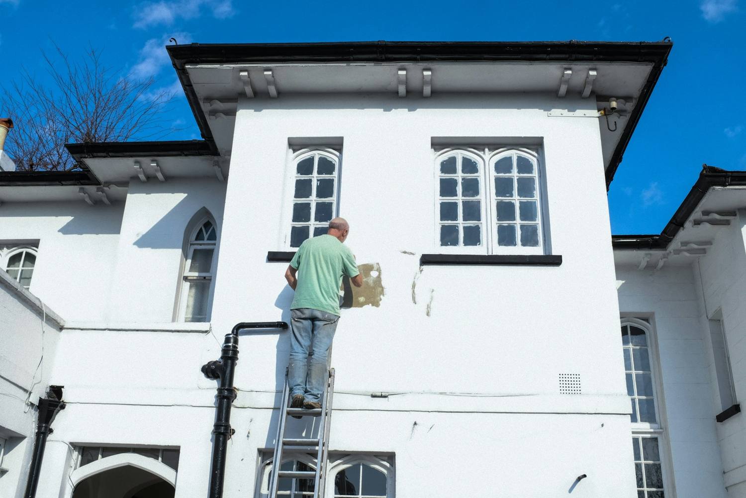 Painter on a ladder patching stucco on a white two-story house