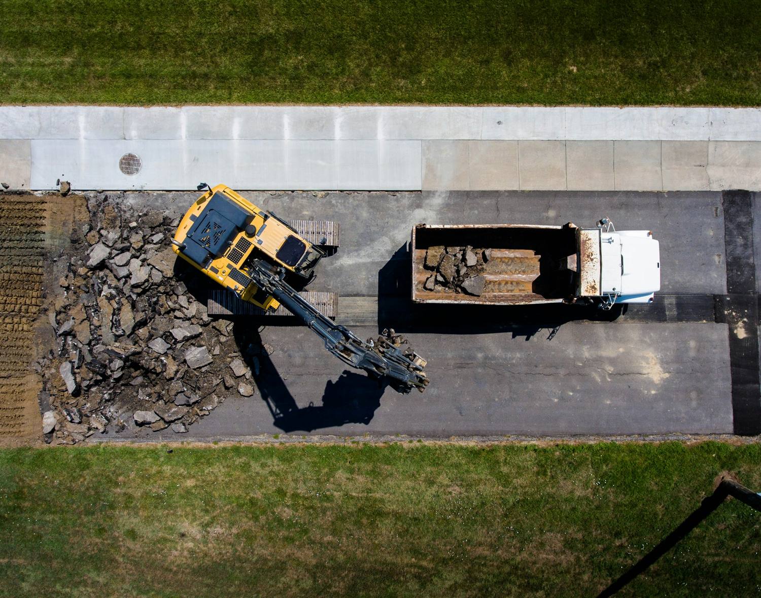 Overhead view of an excavator loading broken asphalt into a dump truck