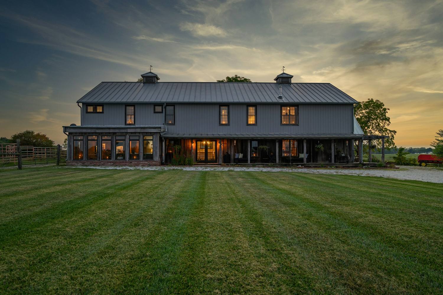 Large barn-style house with dark vertical siding and a standing-seam metal roof at dusk