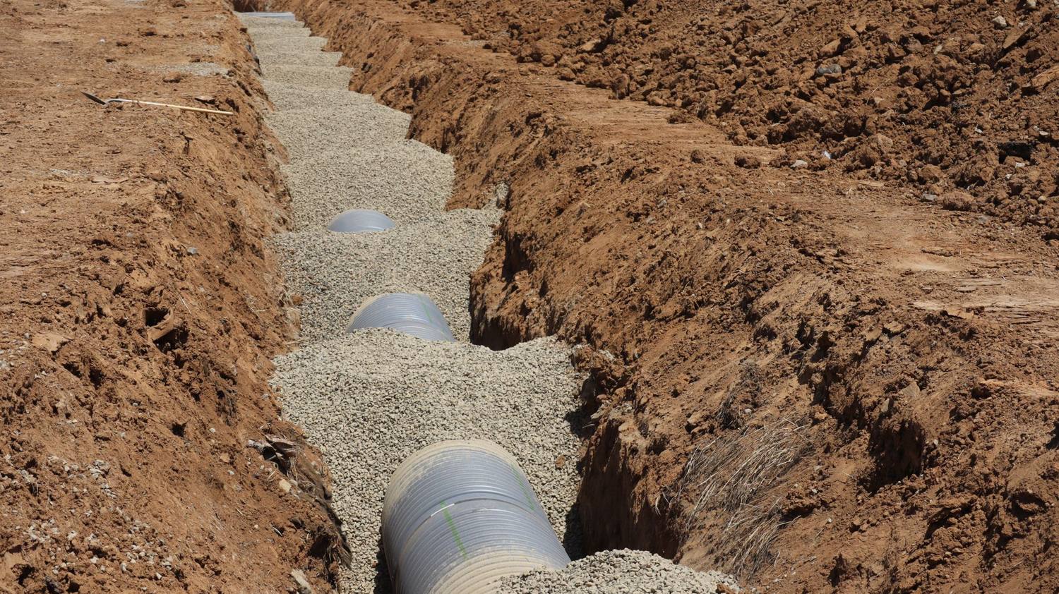 Perforated drain pipe bedded in gravel along the bottom of an open trench